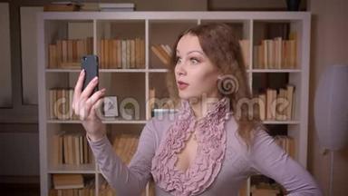 白种人波浪发金发的金发<strong>教师</strong>在智能手机上的<strong>视频</strong>聊天的肖像，微笑着在图书馆。